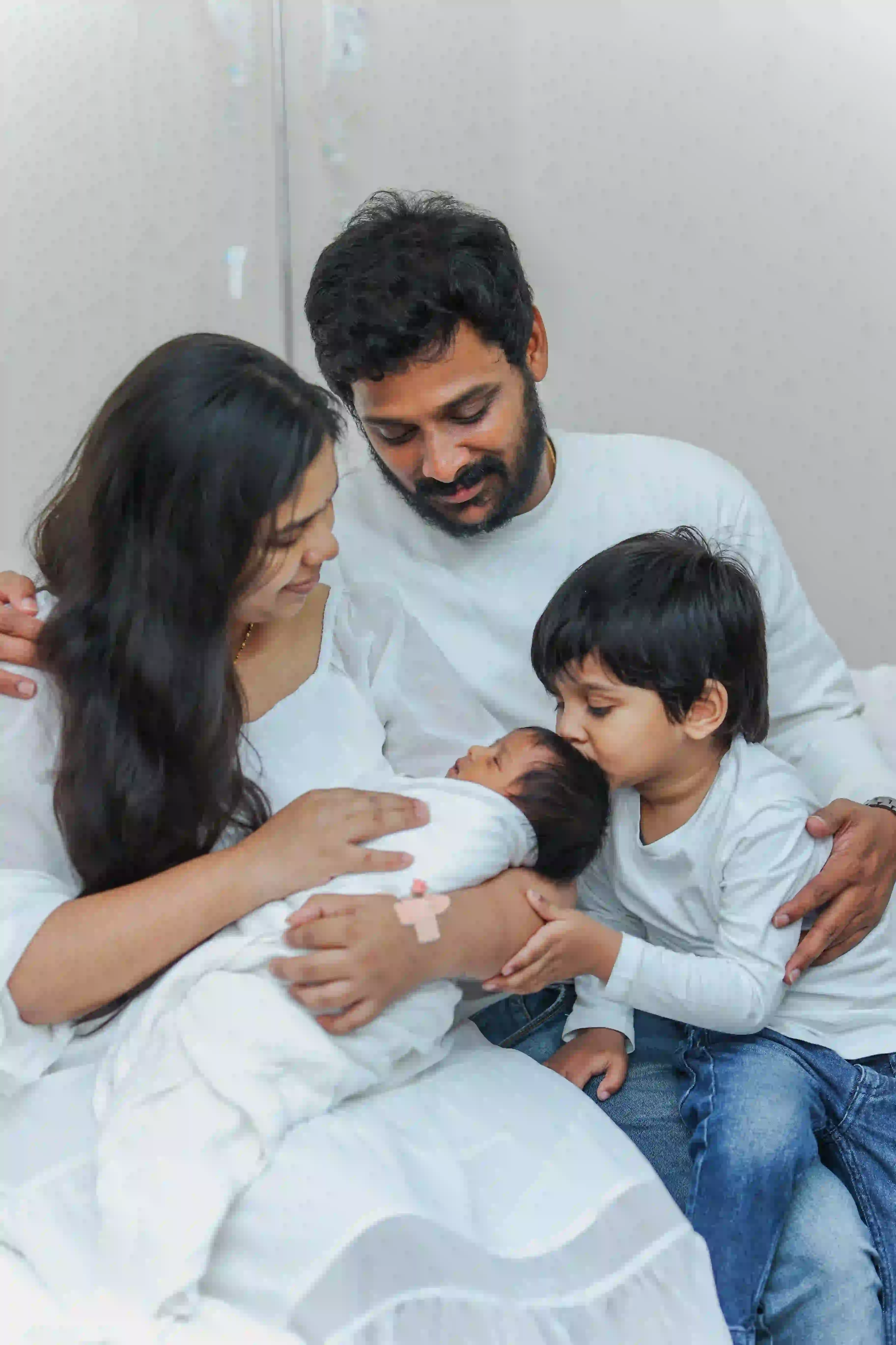Newborn baby being held by parents and older sibling, with the family sharing a heartfelt moment in a hospital room.