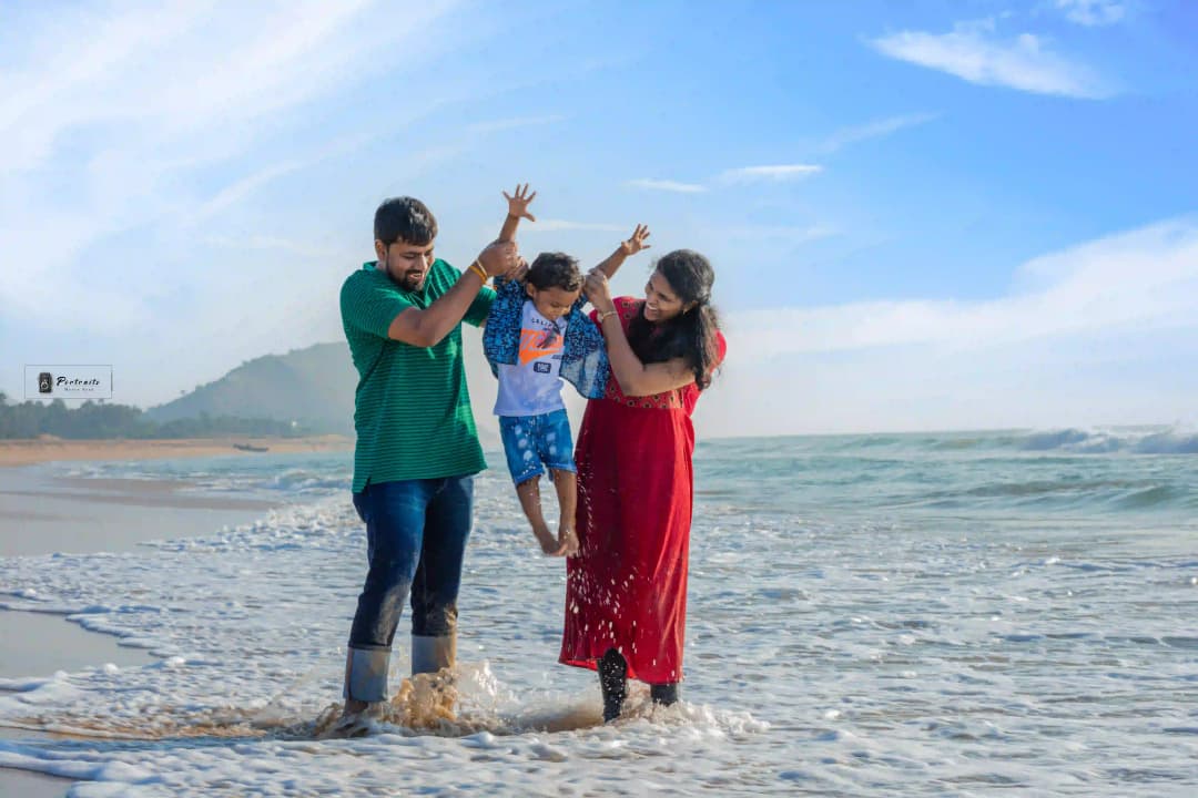 Family having fun at the beach with parents lifting their child in the air while splashing in the waves.