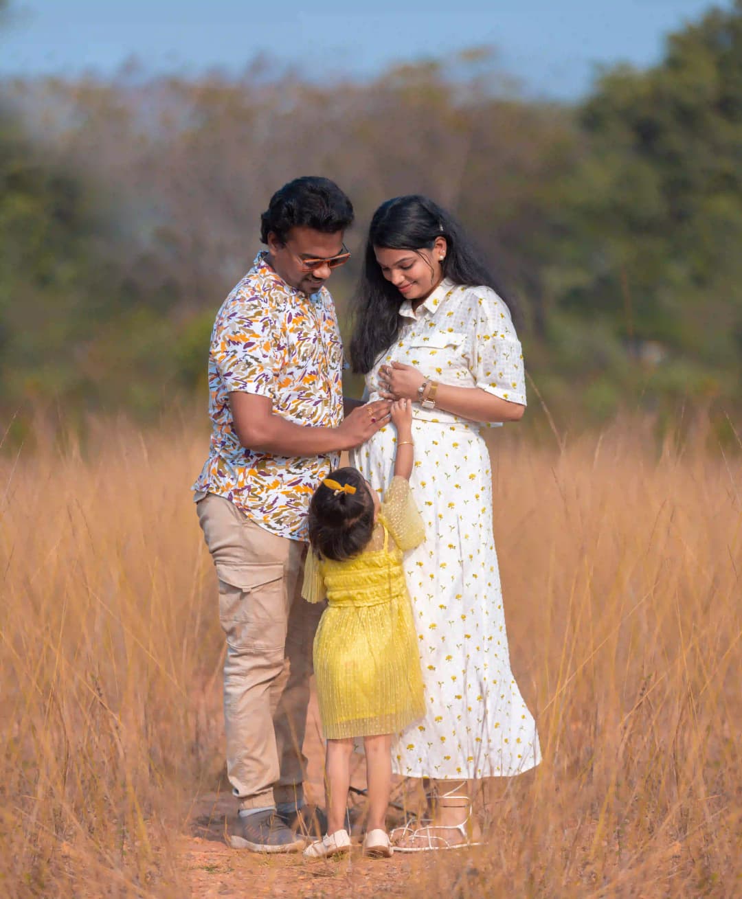 Happy family of three standing in a golden field, sharing a special moment as their child holds their hands.
