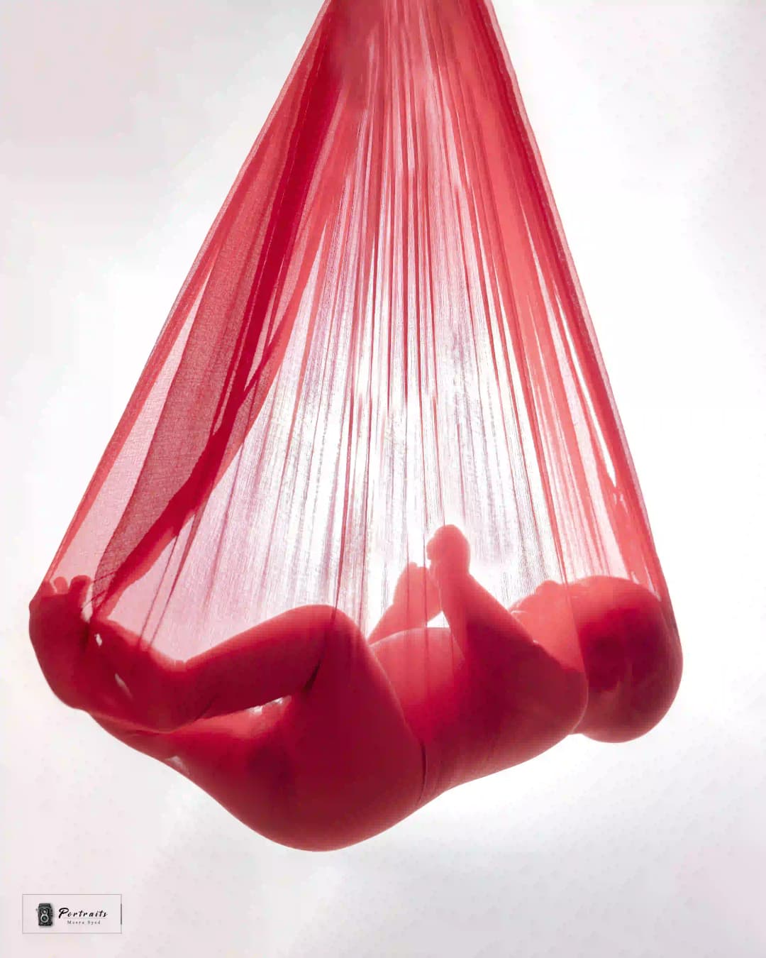 Newborn baby peacefully resting in a red sheer fabric, creating a unique and artistic baby photo.