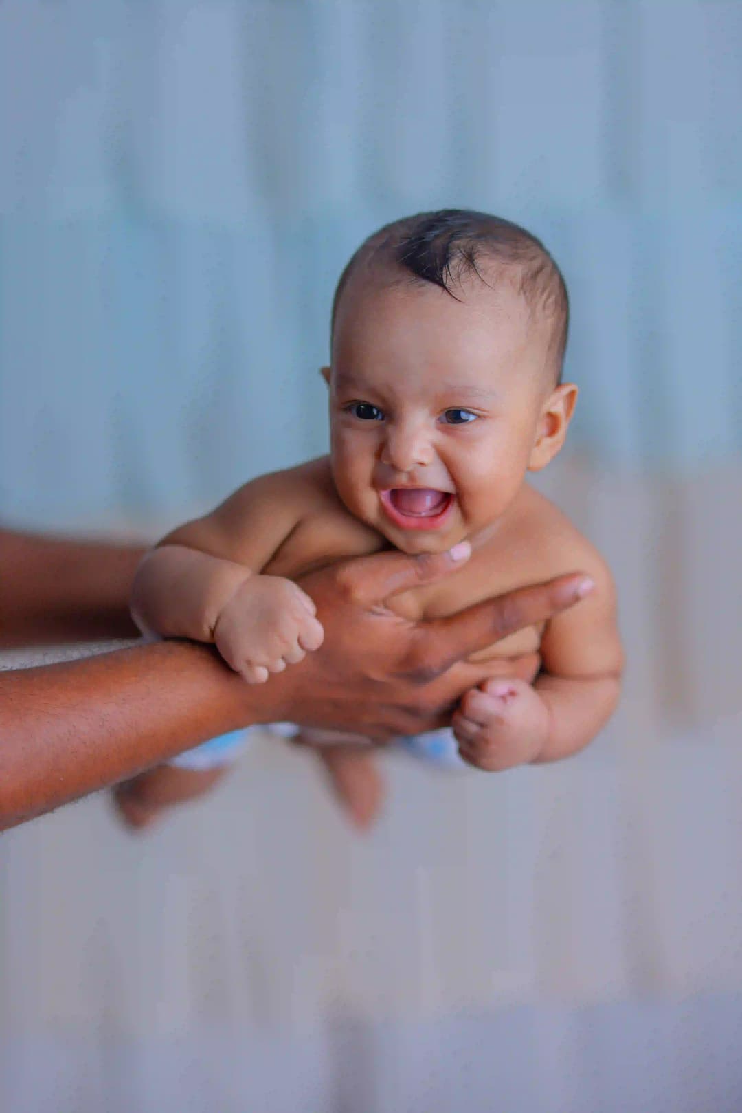 Smiling baby being playfully lifted by an adult, enjoying a joyful moment in a close-up shot.