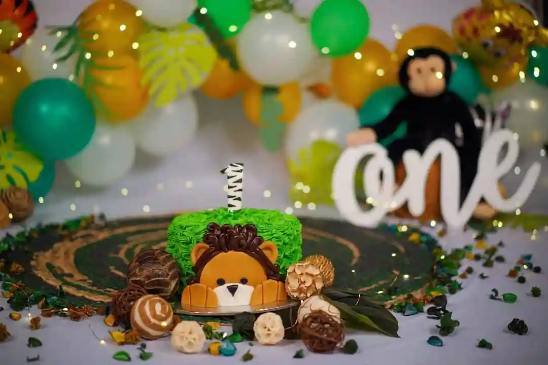 Lion-themed birthday cake with jungle decorations, surrounded by balloons and a 'one' sign, celebrating a child's first birthday.