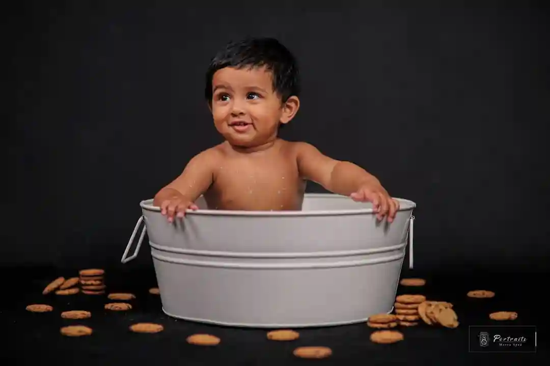 Cute baby sitting in a tub with a playful expression, surrounded by cookies on a black background