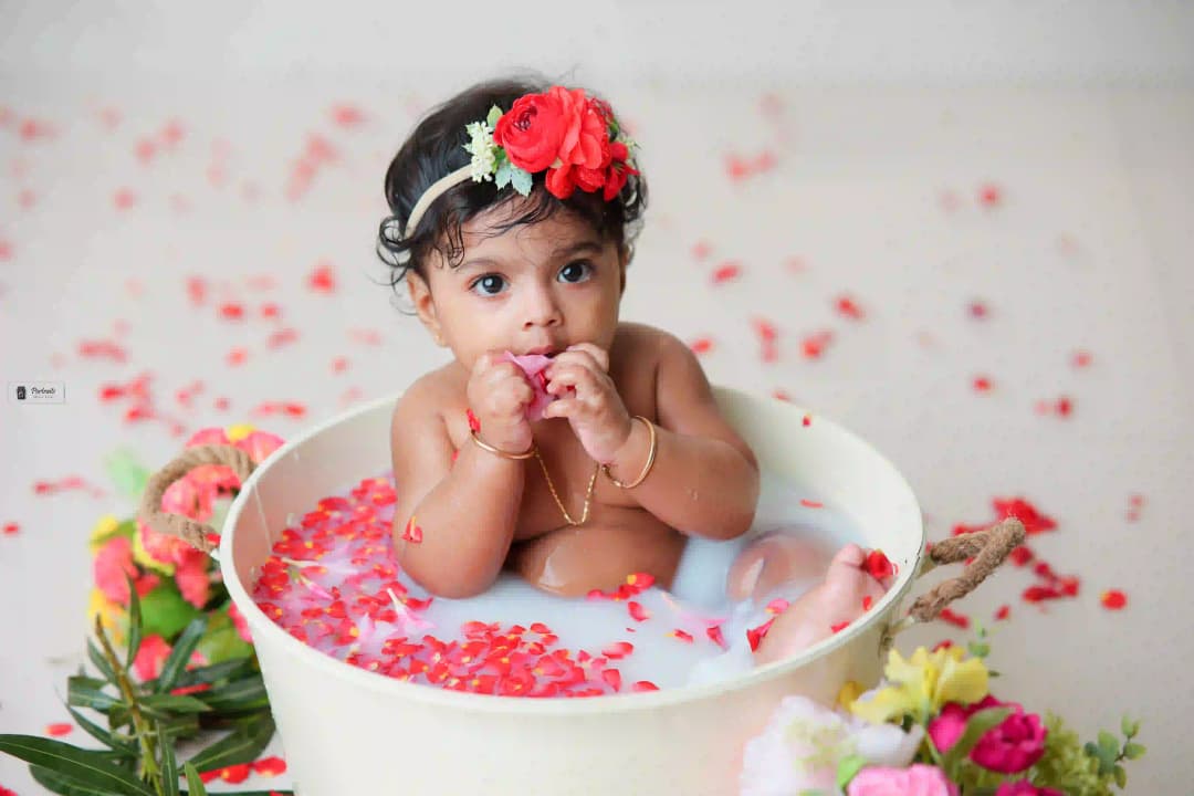 Baby sitting in a milk bath filled with flower petals, wearing a floral headband, creating a serene and beautiful scene.