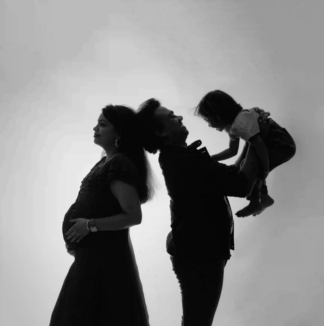 Black and white silhouette of a pregnant mother, father lifting a child, showcasing a beautiful family moment