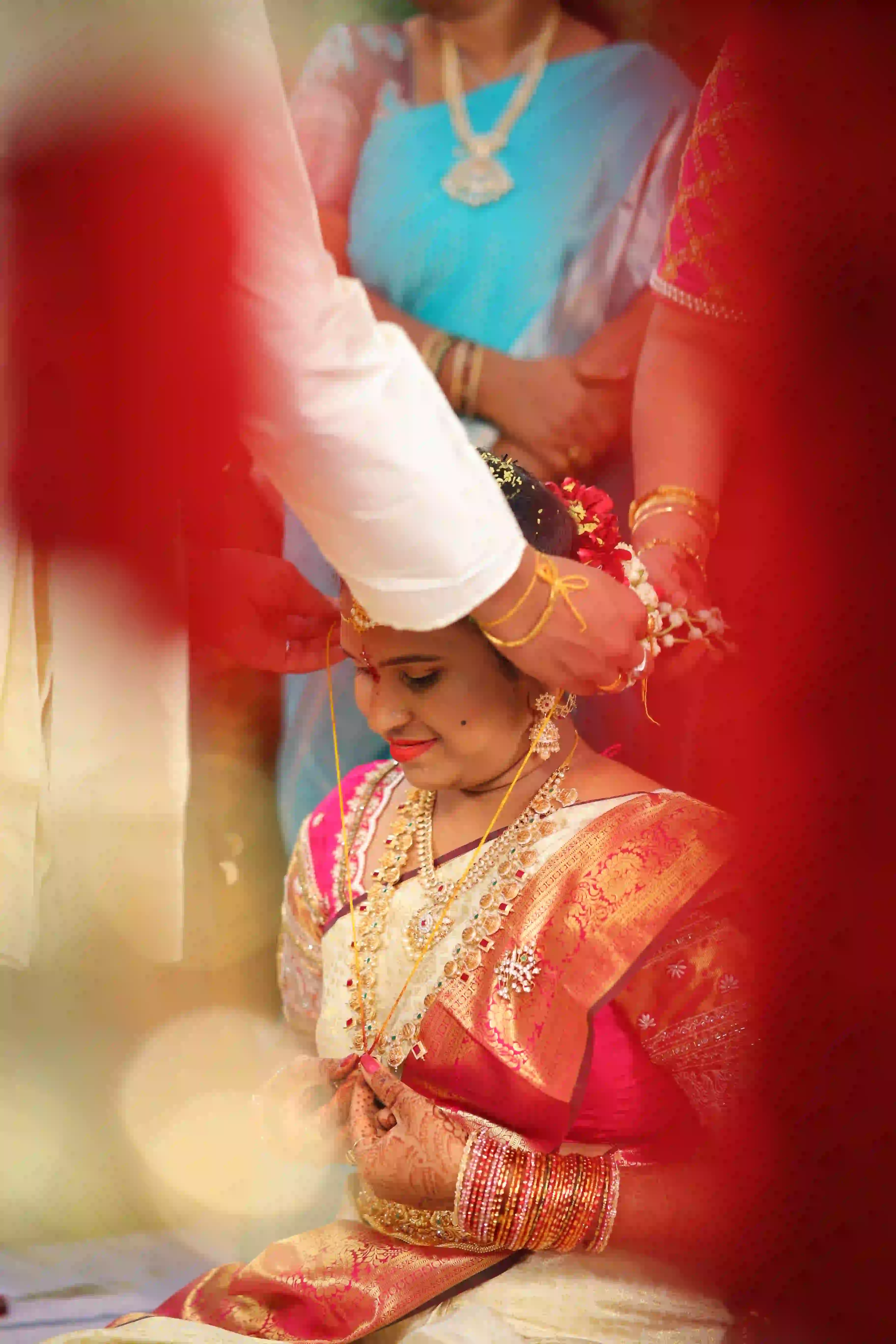 Bride sitting gracefully as she is being adorned with a flower garland during a traditional wedding ceremony.